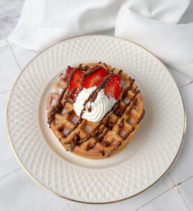 Visão frontal do waffle sem glúten com chantilly, chocolate e morangos