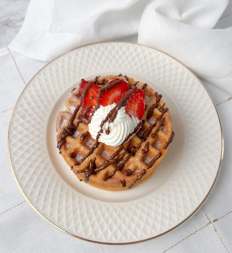 Visão frontal do waffle sem glúten com chantilly, chocolate e morangos